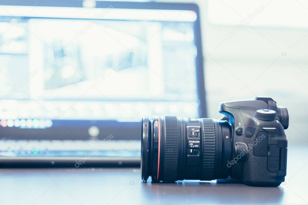 Professional camera with telephoto lens on a table, laptop in the blurry background