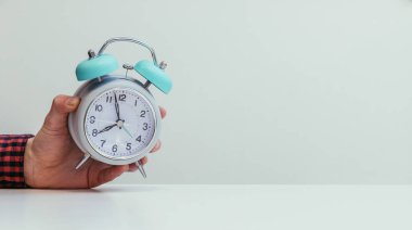 Male hand is holding a retro styled white alarm clock, isolated  clipart