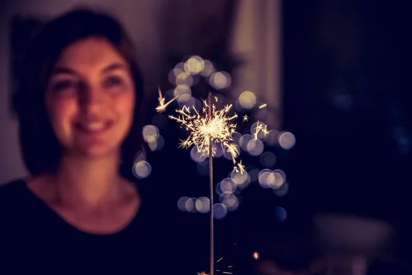 Smiling girl is holding a sparkler in her hand, indoor, lights in background