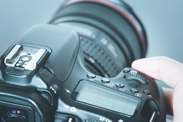 Photographer is holding a professional camera with telephoto lens in his hand, laptop in the blurry background