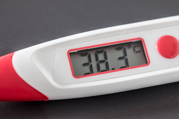 Red fever thermometer with digital display and 38 degrees Celsius lying on the desk