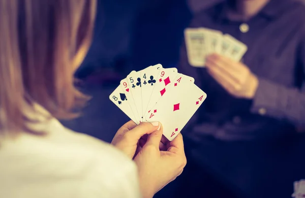 Card playing at home: Friends are sitting on a table. Woman playing cards, man in blurry background.