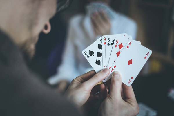 Карты играют дома: Друзья сидят на столе. Мужчина играет в карты, человек на расплывчатом фоне
.