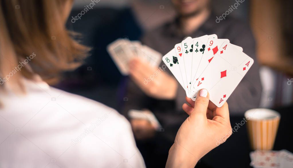 Card playing at home: Friends are sitting on a table. Woman playing cards, man in blurry background.