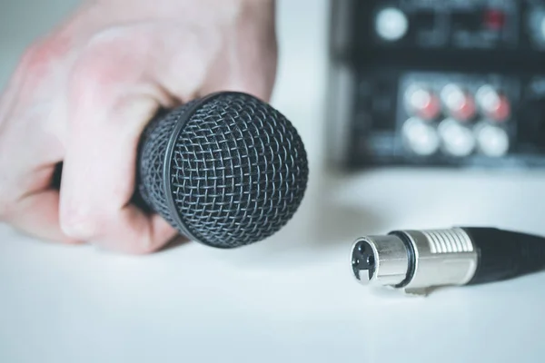 Black microphone holding in hand, and audio cable, mixer in the