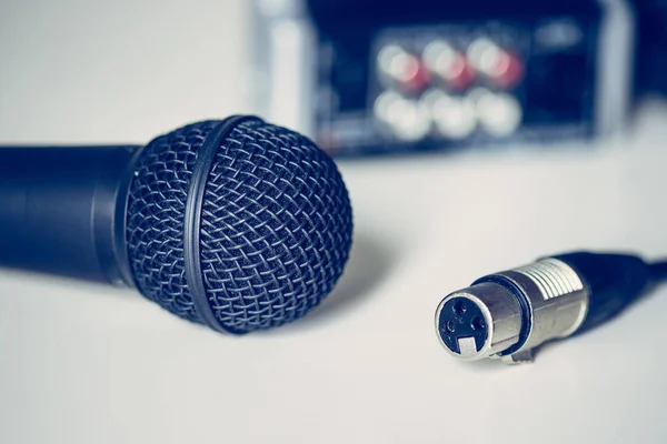 Black microphone and audio cable, mixer in the blurry background — Stock Photo, Image