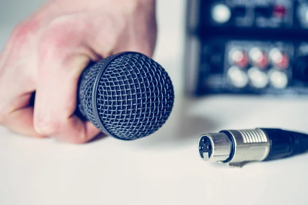 Black microphone holding in hand, and audio cable, mixer in the