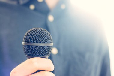 Journalist is holding a microphone in the foreground, blurry bac clipart