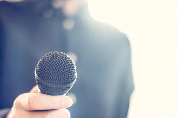 Journalist is holding a microphone in the foreground, blurry bac — Stock Photo, Image