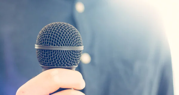 Journalist is holding a microphone in the foreground, blurry bac — Stock Photo, Image