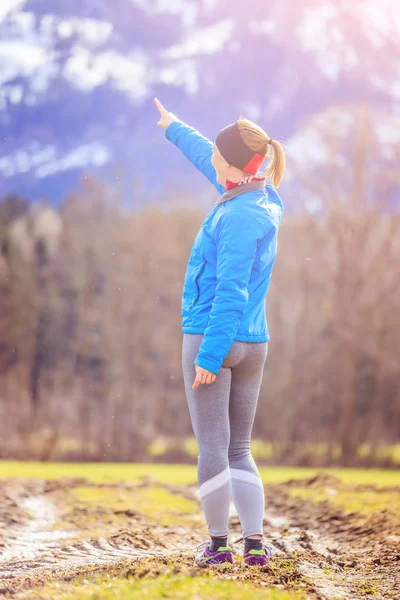 Mujer joven en ropa deportiva está de pie en un campo, señalando somew —  Fotos de Stock