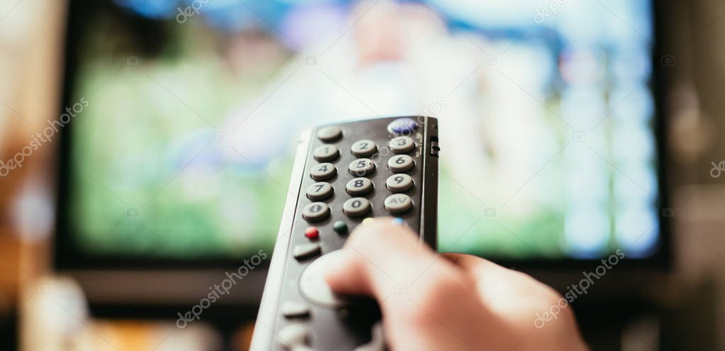 Male hand is holding TV remote control, streaming on a smart TV.