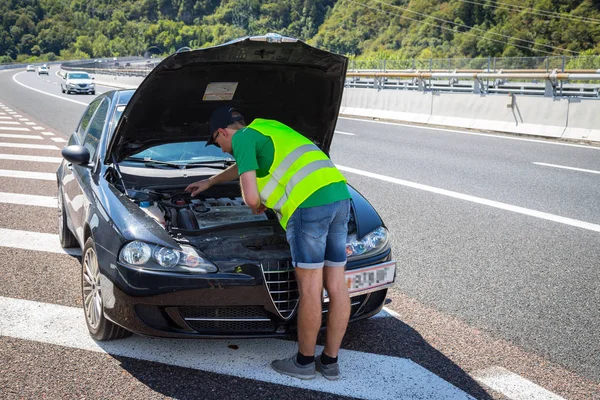 Mechanic in reflective vest is trying to repair a broken-down ca