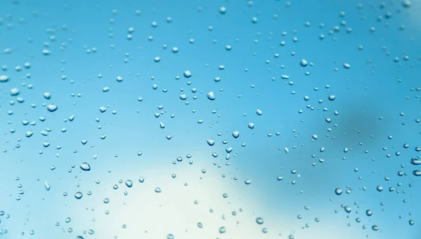 Water druppels op het venster, de blauwe lucht en de wolken in de wazige bac — Stockfoto