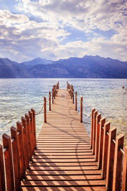 Yaz tatili: Mavi göl suyu üzerinde ahşap rıhtım iskelesi. Bulutlu ev