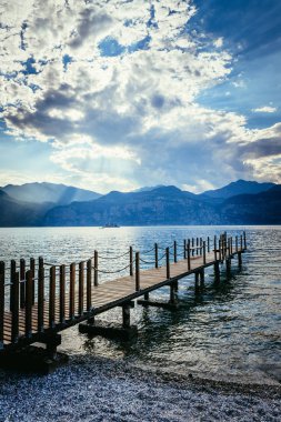 Yaz tatili: Mavi göl suyu üzerinde ahşap rıhtım iskelesi. Bulutlu ev