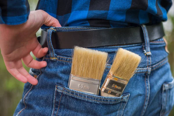 Home handyman: Rear view of a young man with paint brushes in hi — Stock Photo, Image