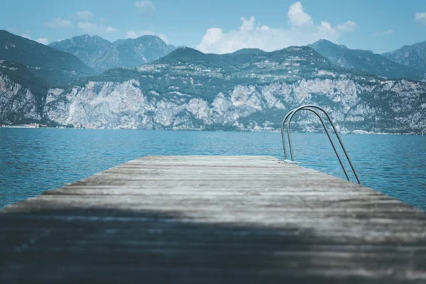 Muelle de madera que se extiende sobre el agua azul del lago, montañas en la — Foto de Stock