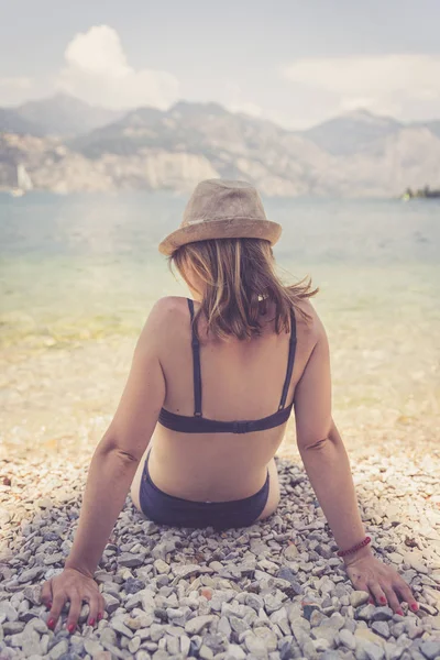 아름다운 젊은 여자 에 비키니 가 앉아 에 이 조약돌 바닷가 a — 스톡 사진