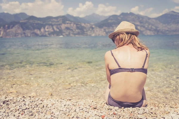 아름다운 젊은 여자 에 비키니 가 앉아 에 이 조약돌 바닷가 a — 스톡 사진