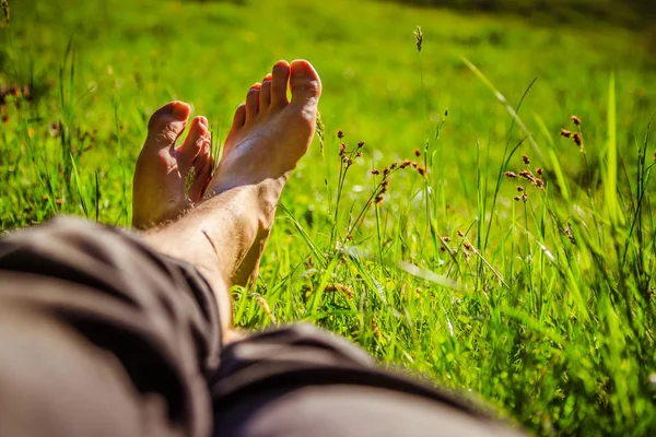 Chlazení v zelené trávě: nohy mladého muže, uklidňující, souhr — Stock fotografie
