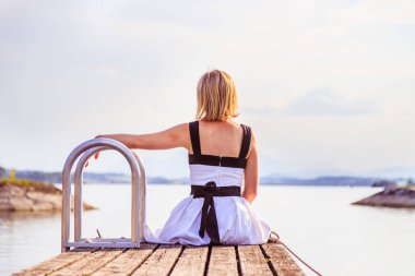 Beyaz elbise ile güzel genç kadın bir footbridg üzerinde oturuyor