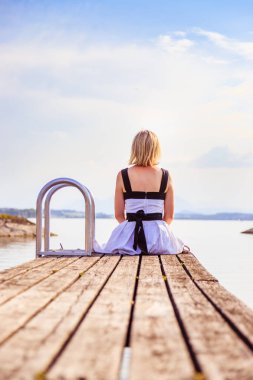 Beyaz elbise ile güzel genç kadın bir footbridg üzerinde oturuyor