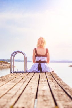 Beyaz elbise ile güzel genç kadın bir footbridg üzerinde oturuyor