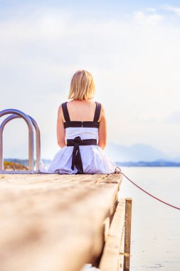 Beyaz elbise ile güzel genç kadın bir footbridg üzerinde oturuyor