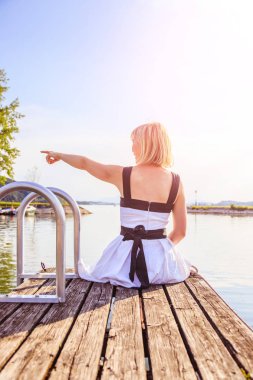 Beyaz elbise ile güzel genç kadın bir footbridg üzerinde oturuyor