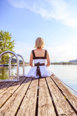 Beyaz elbise ile güzel genç kadın bir footbridg üzerinde oturuyor