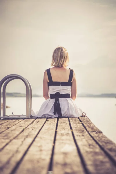 Gyönyörű fiatal nő, fehér ruhában ül egy footbridg — Stock Fotó