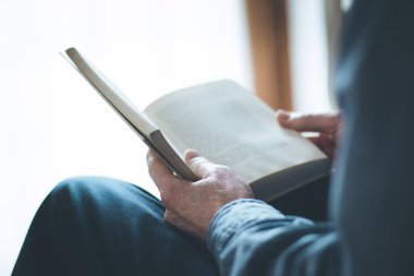 Kıdemli adam evde bir kitap okuyor, seçici odak