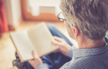 Kıdemli adam evde bir kitap okuyor, seçici odak