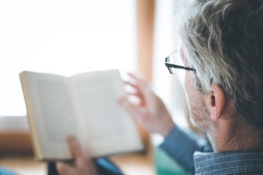 Kıdemli adam evde bir kitap okuyor, seçici odak