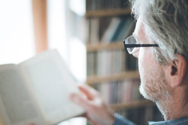 Kıdemli adam evde bir kitap okuyor, seçici odak