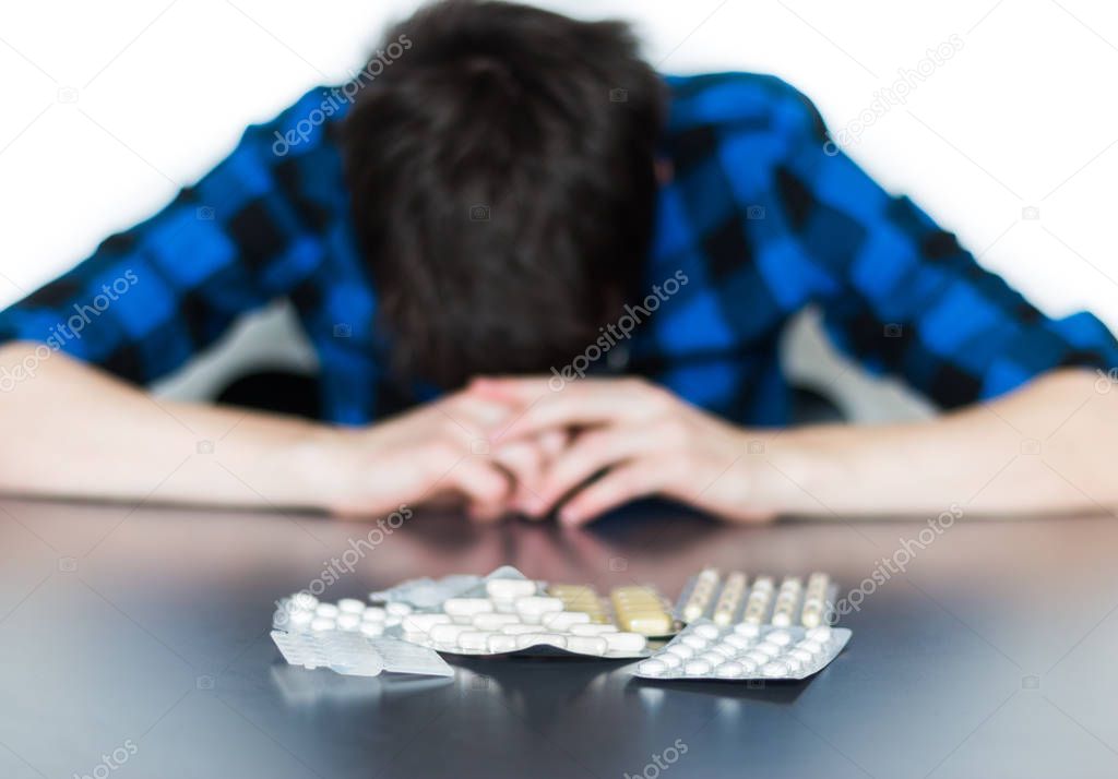 Depressed man taking drugs. Young man sitting on a table, drugs 
