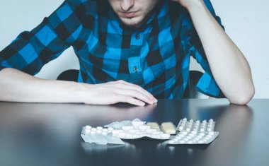 Depressed man taking drugs. Young man sitting on a table, drugs  clipart