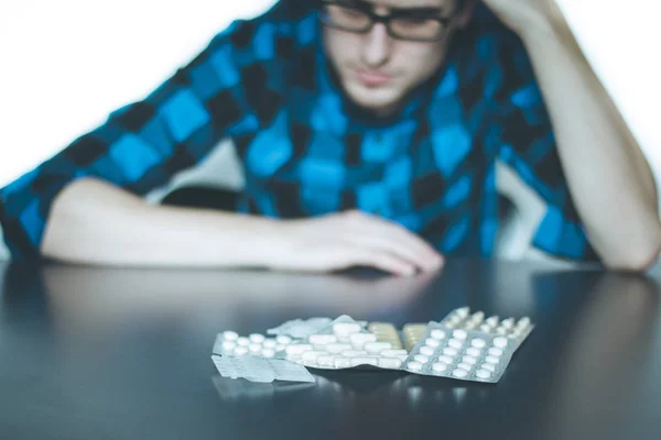 Depressed man taking drugs. Young man sitting on a table, drugs — Stock Photo, Image