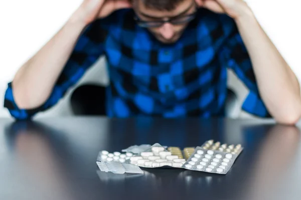 Depressed man taking drugs. Young man sitting on a table, drugs — Stock Photo, Image