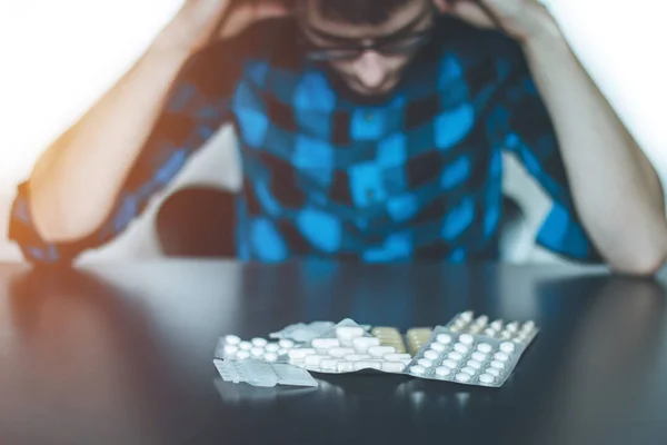 Depressed man taking drugs. Young man sitting on a table, drugs — Stock Photo, Image