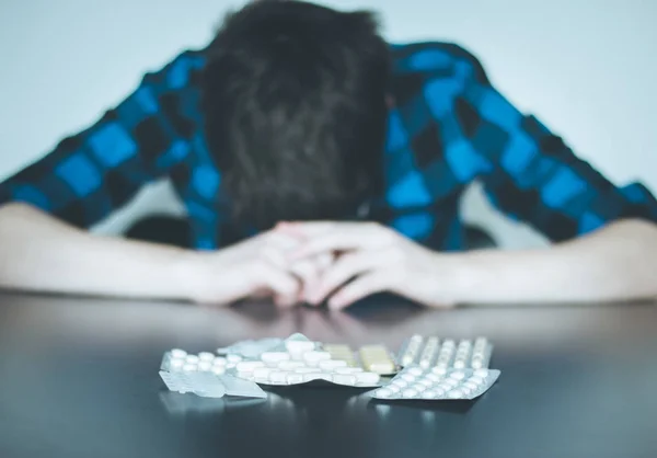 Hombre deprimido tomando drogas. Joven sentado en una mesa, drogas —  Fotos de Stock