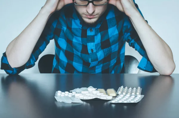 Депресивний чоловік приймає наркотики. Молодий чоловік сидить на столі, наркотики — стокове фото