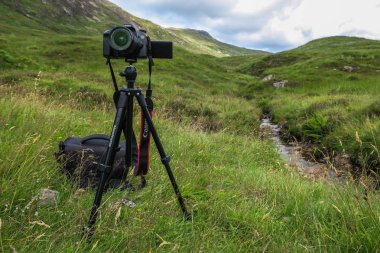 Bir dağ arka planında üç ayaklı kamera.