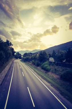 Durgun, dramatik bir yol ve bulutlu bir gökyüzü.