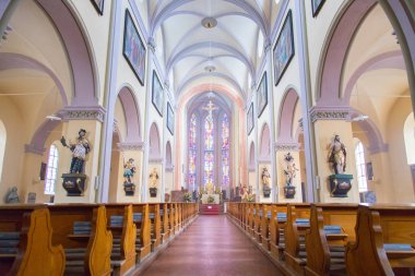 Büyük, modern bir kilisenin içinde sıralar ve haçlar görünür. 