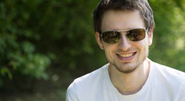 Güneş gözlüklü bir adam dışarıda yeşil çimlerde dinleniyor.