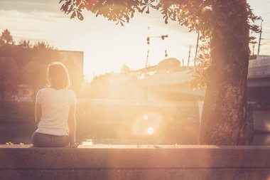 Genç kadın nehrin üzerinde gün batımını izliyor.