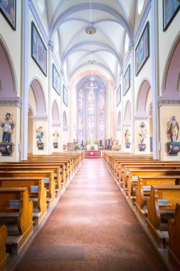 Büyük, modern bir kilisenin içinde sıralar ve haçlar görünür. 