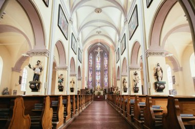 Büyük, modern bir kilisenin içinde sıralar ve haçlar görünür. 